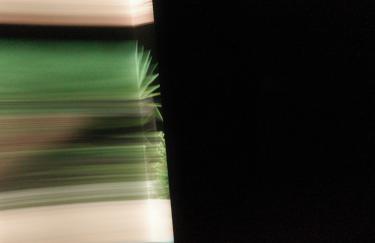 „Ein teilweise verdeckter Blick in einen Raum. Grüne Linien verlaufen entlang der Wände und werden in einer Ecke – ähnlich wie Lichtstrahlen – umgelenkt.