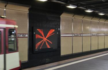 A platform at the Düsseldorf Central Station subway station where an advertising screen displays a video work by Yoora Park. On the left, A track at the Düsseldorf Hauptbahnhof subway station, featuring an advertising screen displaying a video work by Yoora Park. To the left, part of a departing subway train is visible.