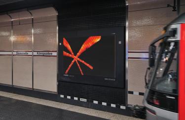 A platform at the Steinstraße/Königsallee subway station in Düsseldorf where an advertising screen displays a video work by Yoora Park. To the right, part of an arriving subway train is visible.