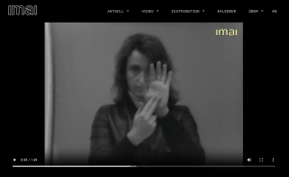 Valie Export, Sehtext: Fingergedicht, 1968/73 im Online-Archiv des IMAI, 2024 Ein Videostill von Valie Export, eingebettet in eine Online-Plattform. Die Künstlerin blickt in die Kamera und formt ein Zeichen mit den Händen. Es ist das Zeichen für den Buchstaben „n“ im Zweihand-Fingeralphabet. Intendiert ist aber vermutlich der Buchstabe „m“.