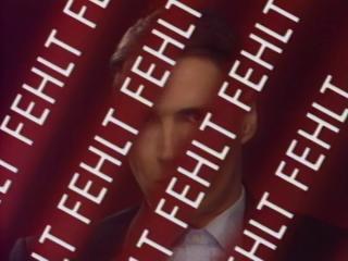 A white person perceived as male, wearing a suit, standing in front of a red background, partially obscured by tape bearing the white word "MISSING."