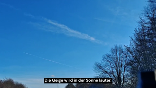 Blauer Himmel mit Kondensstreife über offener Landschaft mit kahlen Bäumen, Perspektive aus Bewegung, unten Untertitel „Die Geige wird in der Sonne lauter.“