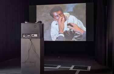 Marcel Odenbachs zweikanalige Videoinstallation in der Filmwerkstatt Düsseldorf. Am Ende des Raumes hängt eine große Projektionswand auf der eine Szene mit Jimmy Stewart in Blackface-Makeup von Alfred Hitchcocks „The Man Who Knew Too Much“ (1956) abgespielt wird. Davor steht ein CRT Monitor auf einem Sockel in Richtung der Leinwand. Auf dem Boden ist ein selbstgemachtes Blindenleitsysteme installiert, das in die Ausstellung hineinführt.