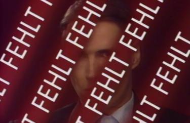 A white person perceived as male, wearing a suit, standing in front of a red background, partially obscured by tape bearing the white word "MISSING."