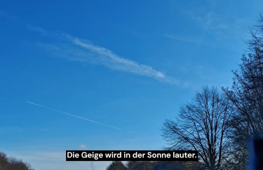 Blauer Himmel mit Kondensstreife über offener Landschaft mit kahlen Bäumen, Perspektive aus Bewegung, unten Untertitel „Die Geige wird in der Sonne lauter.“